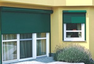 Nahaufnahme von einem gelben Haus mit heruntergelassenen grünen Rolläden