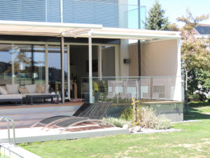 modernes Einfamilienhaus in Rickenbach mit einer grossen Terrasse und Gartenbereich. Auf der Terrasse sind die senkrechten Sonnenstoren heruntergelassen.
