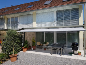 Ein Haus in Horw mit Terrassen- und Gartenbereich. Zusehen sind drei Fenster im oberen Stock vom Gebäude. Zwei Fenster mit geschlossenen und eine mit halb geöffneten Lamellenstoren.