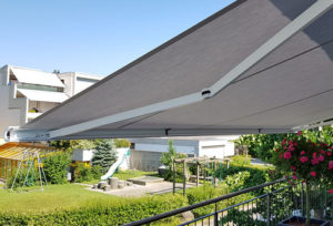 Seitenaufnahme von einer grauen Sonnenstore. Dahinter ist ein idyllisches Wohnquartier mit Spielplatz zusehen.