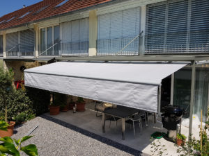 Zusehen ist der Gartenplatz von einem Einfamilienhaus in Horw, welcher von einer Sonnenstore mit heruntergelassenem Volant, geschützt wird.
